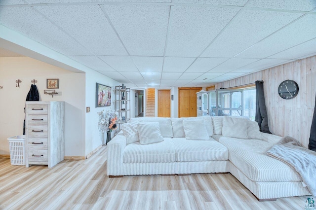 living room with light wood-type flooring, a drop ceiling, and wooden walls