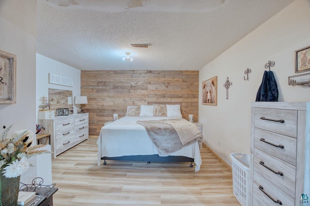 bedroom featuring light wood-type flooring, wood walls, and a textured ceiling