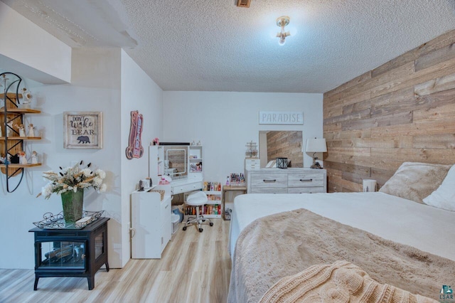 bedroom with a textured ceiling, light hardwood / wood-style floors, and wooden walls