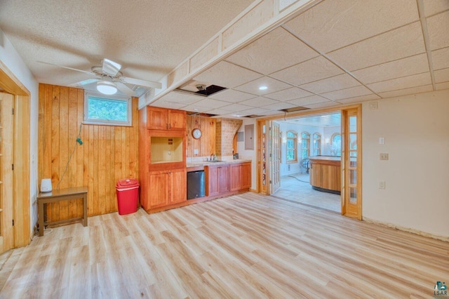 kitchen featuring ceiling fan, wood walls, black dishwasher, and light hardwood / wood-style floors