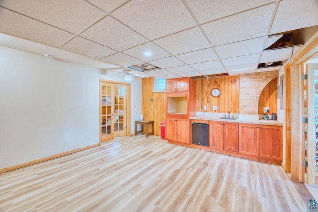 bar featuring dishwasher, sink, wood walls, a drop ceiling, and light hardwood / wood-style flooring