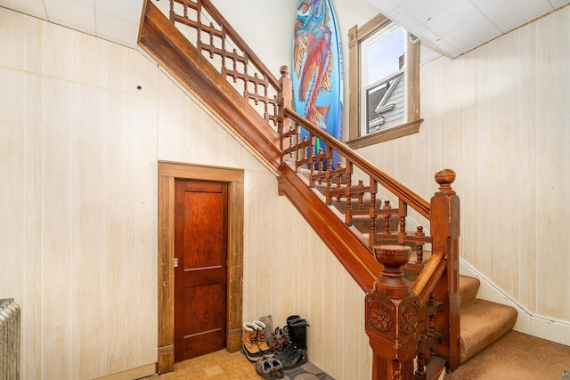 stairway featuring carpet, wooden walls, and radiator heating unit