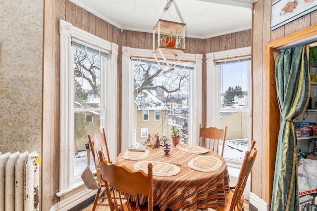 dining room featuring radiator, wood walls, a healthy amount of sunlight, and ornamental molding