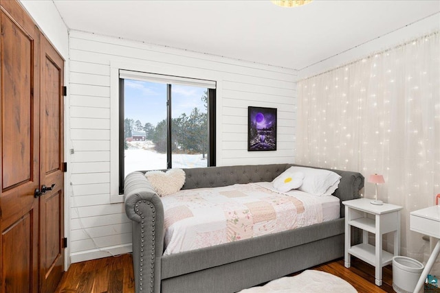 bedroom with a closet, wood walls, and dark wood-type flooring