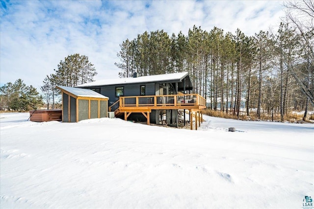 snow covered back of property featuring a wooden deck and a hot tub