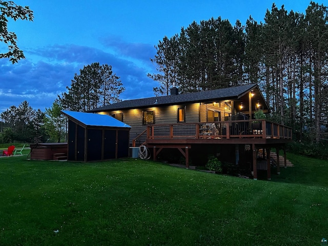 back house at dusk with a deck, a hot tub, and a lawn