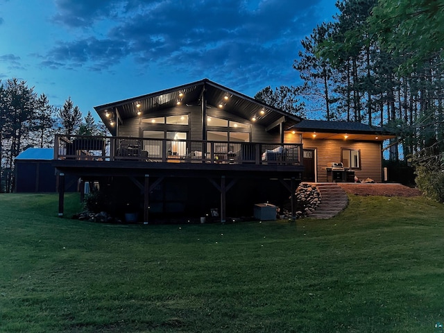 back house at dusk featuring a deck and a lawn