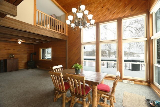 dining area featuring a towering ceiling, wooden walls, carpet floors, a wood stove, and a chandelier