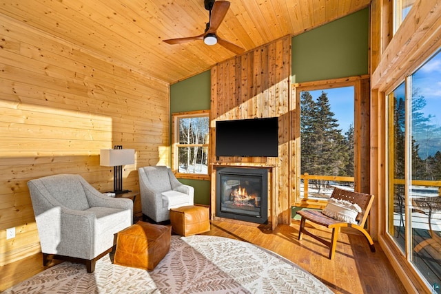 living area with wood-type flooring, wooden ceiling, ceiling fan, and wood walls