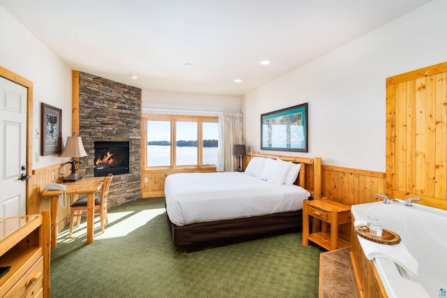 bedroom with wood walls, a stone fireplace, dark colored carpet, and a water view