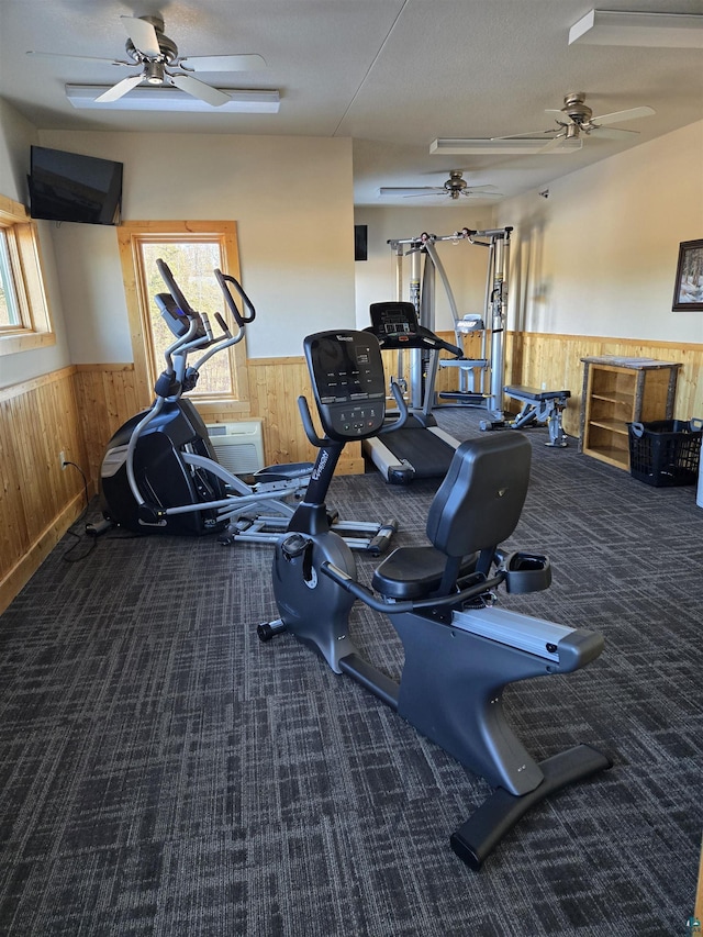 exercise room featuring carpet, a wealth of natural light, ceiling fan, and wood walls