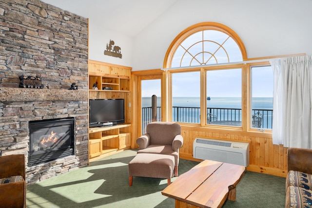 living room featuring wooden walls, a wall mounted air conditioner, carpet floors, built in shelves, and a stone fireplace