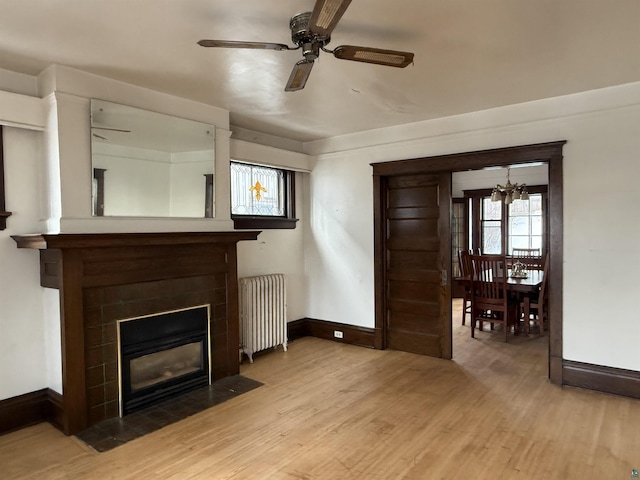 unfurnished living room featuring ceiling fan with notable chandelier, radiator heating unit, and light hardwood / wood-style floors