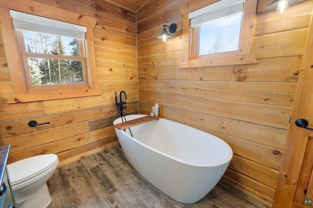 bathroom featuring wood-type flooring, a washtub, wooden walls, and toilet