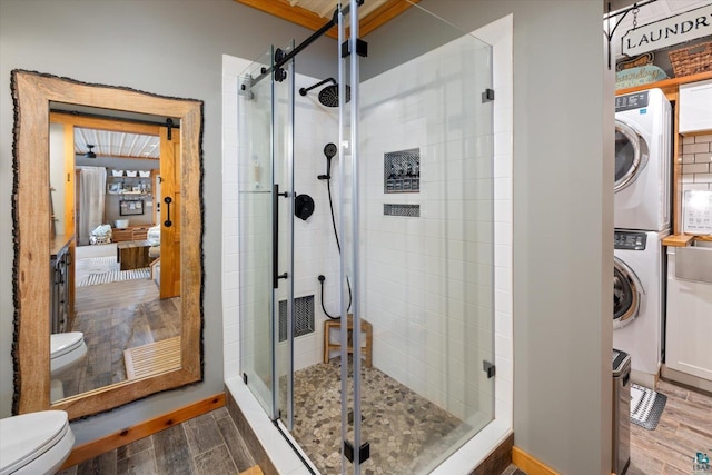 bathroom with stacked washer / drying machine, an enclosed shower, and toilet