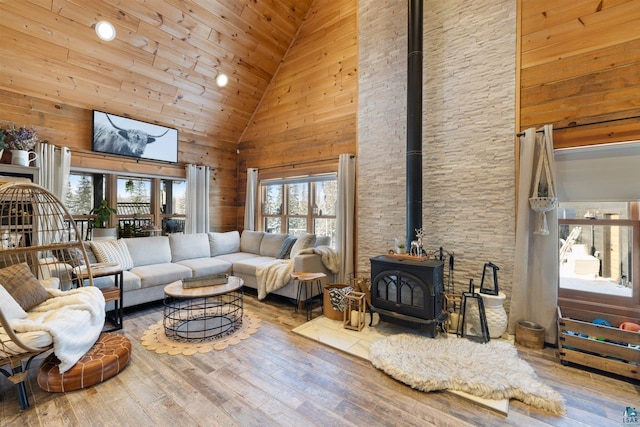 living room featuring wood-type flooring, wooden walls, high vaulted ceiling, and a wood stove