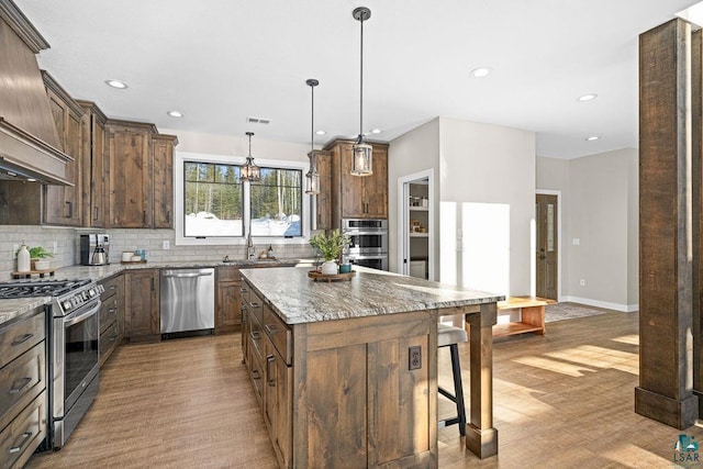 kitchen with hanging light fixtures, light stone countertops, appliances with stainless steel finishes, and a center island