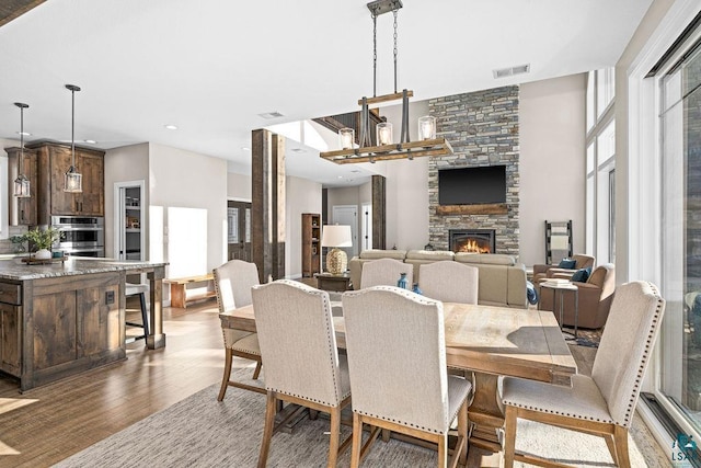 dining area with a stone fireplace, hardwood / wood-style floors, and a notable chandelier