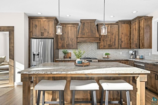 kitchen featuring premium range hood, appliances with stainless steel finishes, a kitchen island, and pendant lighting