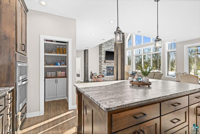 kitchen with dark wood-type flooring, a stone fireplace, a kitchen island, pendant lighting, and stainless steel double oven