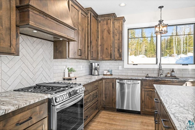 kitchen with sink, appliances with stainless steel finishes, plenty of natural light, light stone counters, and custom exhaust hood