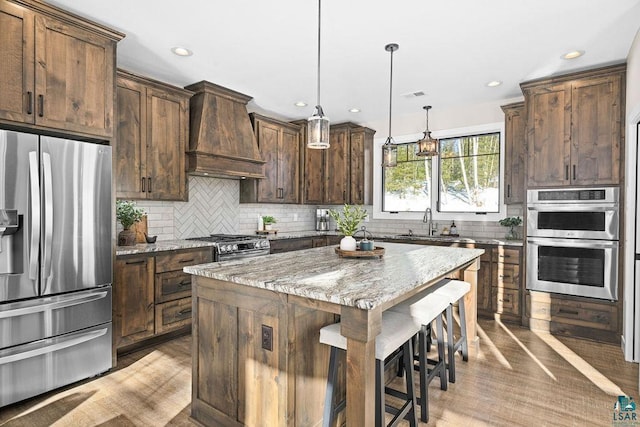 kitchen with hanging light fixtures, stainless steel appliances, a center island, light stone counters, and custom range hood