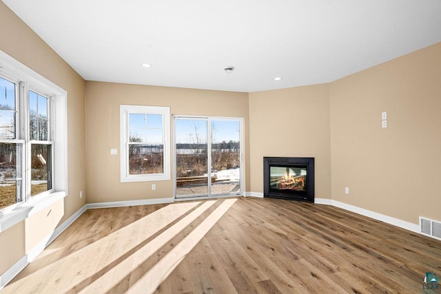 unfurnished living room with light wood-type flooring, a wealth of natural light, and a multi sided fireplace