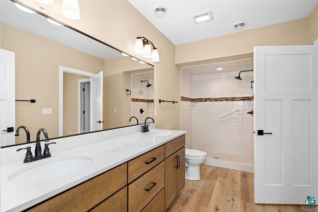 bathroom with wood-type flooring, toilet, vanity, and a tile shower