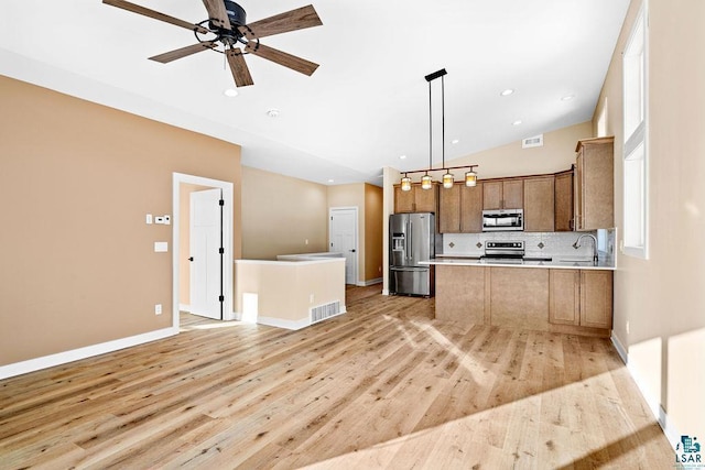 kitchen with pendant lighting, appliances with stainless steel finishes, backsplash, vaulted ceiling, and light wood-type flooring