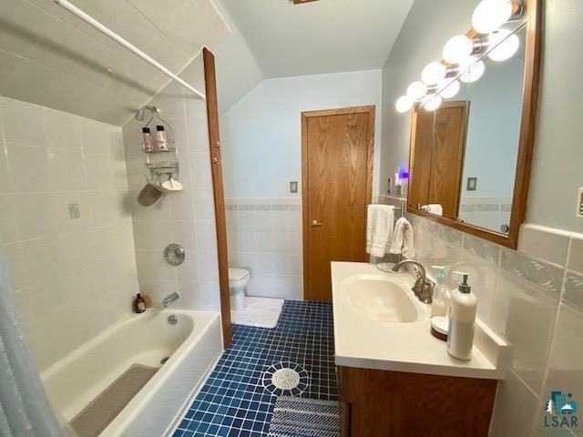 full bathroom featuring toilet, vaulted ceiling, tile walls, vanity, and tiled shower / bath combo