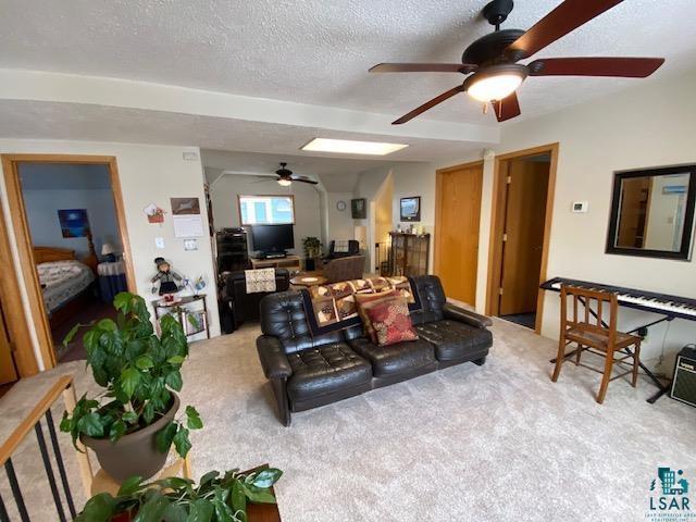 living room with ceiling fan, carpet floors, and a textured ceiling