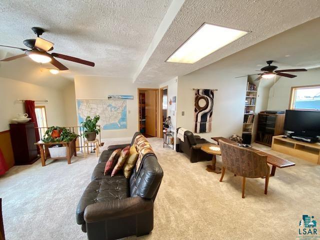 living room with ceiling fan, lofted ceiling, light colored carpet, and a textured ceiling