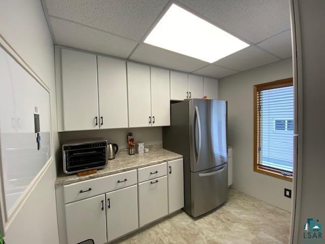 kitchen with stainless steel refrigerator, a drop ceiling, and white cabinets