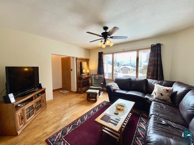 living room with ceiling fan, a textured ceiling, and light wood-type flooring