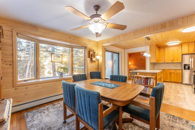 dining room featuring wooden walls, ceiling fan, baseboard heating, light hardwood / wood-style floors, and a textured ceiling