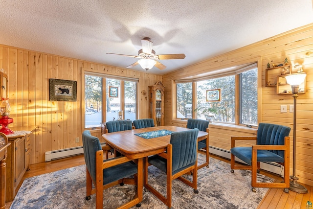 dining room with ceiling fan, light hardwood / wood-style floors, a textured ceiling, and a baseboard heating unit