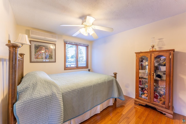 bedroom featuring ceiling fan, a wall mounted air conditioner, hardwood / wood-style floors, and a textured ceiling