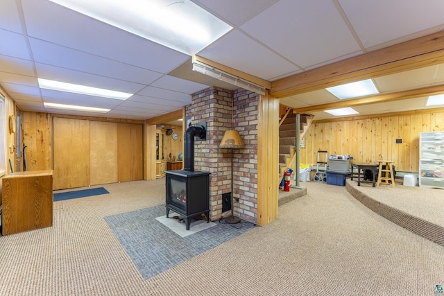 basement with carpet floors, a wood stove, a drop ceiling, and wood walls