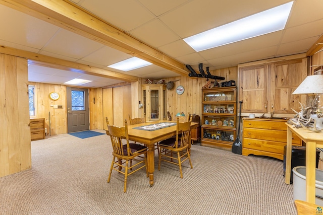 dining area with a paneled ceiling, light carpet, and wooden walls