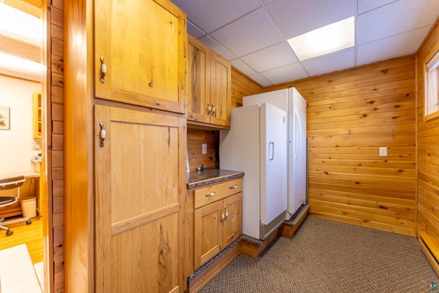 kitchen with white fridge, a paneled ceiling, carpet, and wooden walls