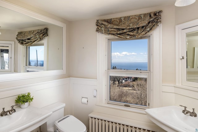 half bathroom featuring radiator, a wainscoted wall, a sink, and toilet