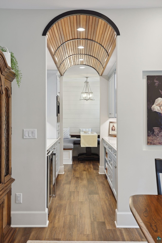 corridor with lofted ceiling, dark hardwood / wood-style floors, a notable chandelier, and beverage cooler