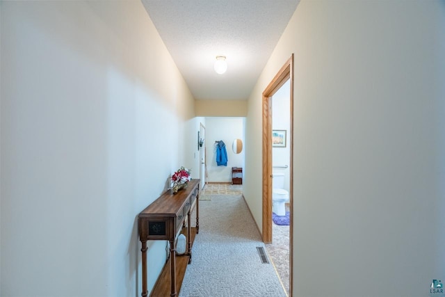 hall with light carpet and a textured ceiling