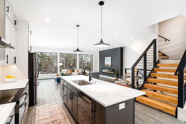 kitchen with pendant lighting, sink, white cabinets, light stone countertops, and a center island with sink