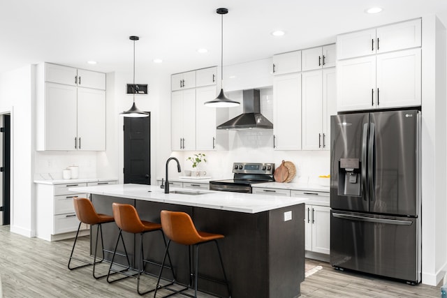 kitchen featuring wall chimney exhaust hood, sink, white cabinetry, an island with sink, and stainless steel appliances