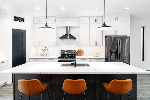 kitchen featuring white cabinetry, a center island with sink, appliances with stainless steel finishes, light stone countertops, and wall chimney range hood