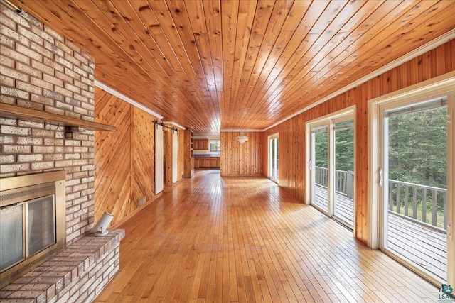 unfurnished living room featuring wood ceiling, wooden walls, a fireplace, and light wood-type flooring