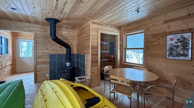 dining space featuring wood ceiling, wood walls, light hardwood / wood-style floors, and a wood stove