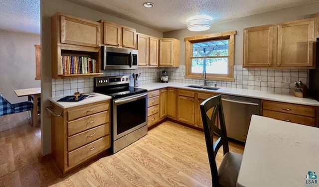 kitchen featuring tasteful backsplash, sink, stainless steel appliances, a textured ceiling, and light hardwood / wood-style flooring