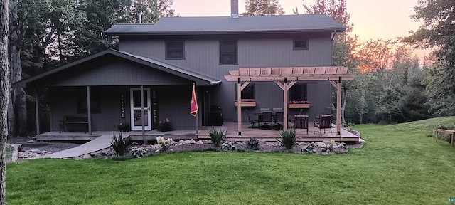 back house at dusk featuring a wooden deck, a pergola, and a lawn